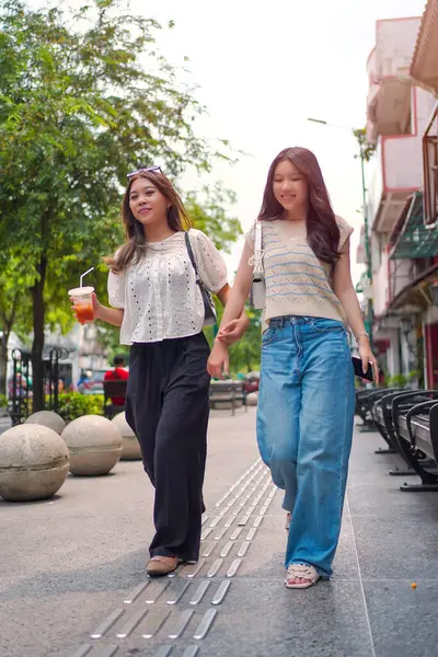 İki neşeli Asyalı kadın şehrin kaldırımında el ele yürüyorlar. Sohbet ederken ve gülümserken, şehir ortamında güneşli bir günün tadını çıkarırken buzlu bir içki içilir..