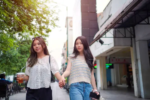 İki neşeli Asyalı kadın şehrin kaldırımında el ele yürüyorlar. Sohbet ederken ve gülümserken, şehir ortamında güneşli bir günün tadını çıkarırken buzlu bir içki içilir..