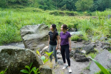 Aktif giyimli iki Asyalı kadın, sürdürülebilir bir yaşam tarzının parçası olarak spor, egzersiz ve doğayı kucaklayan gür orman patikalarını keşfediyorlar..