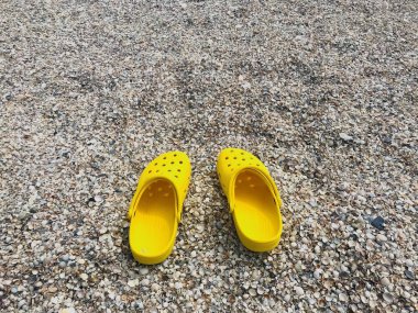 Sarı plaj ayakkabıları, arka planda timsah ayakkabıları. Tatil konsepti. Deniz kıyısında plaj ayakkabıları, deniz kenarında tatil..