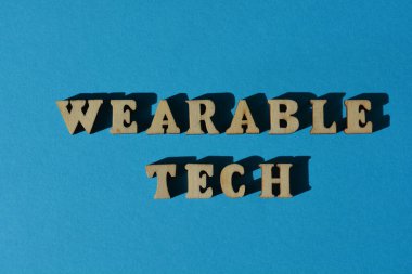 Giyilebilir Teknoloji, mavi arkaplanda izole edilmiş ahşap alfabe harfleri.