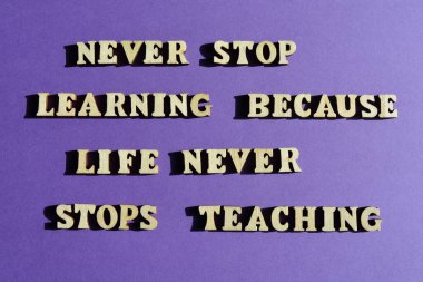 Asla öğrenmeyi bırakma çünkü hayat öğretmeyi asla bırakmaz, motivasyon cümlesi ahşap alfabede mor arka planda izole edilmiş harflerle.