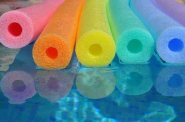 Gökkuşağı renginde polietilen havuz erişteleri mavi fayanslı yüzme havuzunda yüzüyor, yaz havası...