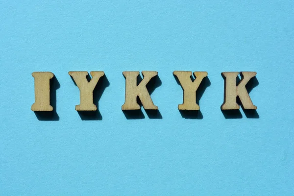 IYKYK, acronym for If You Know You Know in wooden alphabet letters isolated on blue background as banner headline
