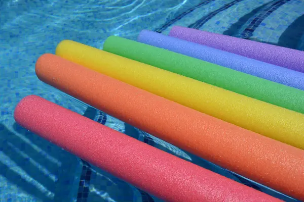 stock image Colourful rainbow pool noodles floating on water in swimming pool, happy summer holiday vibes