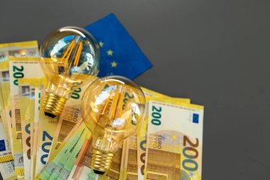 Elektrik faturası. Koyu gri arka planda ampuller ve avro banknotları ve AB bayrağı. Enerji krizi sembolleri. Artan elektrik fiyatları. Avrupa 'da elektrik faturaları.. 