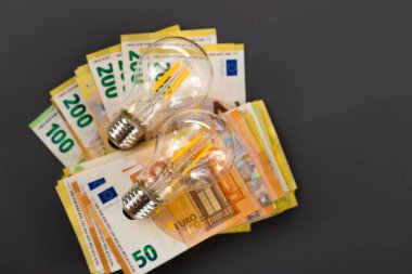 Enerji sektöründeki kriz. AB 'de elektrik maliyetleri. Elektrik faturalarının ödenmesi. Koyu gri arka planda ampuller ayarlandı ve avro banknotları belirlendi. 