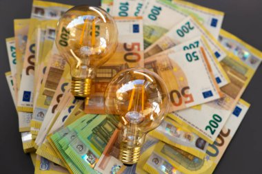 AB 'de elektrik maliyetleri. Elektrik faturalarının ödenmesi. Koyu gri arka planda ampuller ve avro banknotları belirlendi. Enerji sektöründeki kriz. Artan elektrik fiyatları. Elektrik faturaları ödeme. 