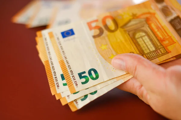 Euro banknotes in hands close-up.50 euro banknotes in hand on a burgundy background. Expenses and incomes in European countries.Recalculation of money.Cash payments and expenses