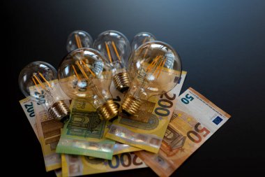 Elektrik faturaları. Avrupa 'da elektrik fiyatları. Ampuller belirlendi ve avro banknotları siyah bir arkaplanda. Enerji sektörü kavramında kriz. Enerji krizi sembolü