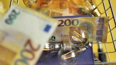 Elektrik faturalarının ödenmesi. El, sarı arka planda bir süpermarket tramvayına avro para koyuyor. Görüntü yukarıdan, hareketler düşük. AB ülkelerinde elektrik maliyetleri. Yüksek kalite 4k görüntü