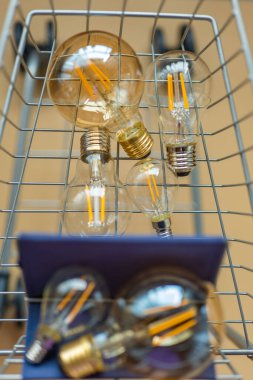 Elektrik satın alımı. Bir alışveriş arabasında bir sürü elektrik lambası. Enerji tüketimi ve ödemesi. Bej bir arka planda süpermarket tramvayında ampuller..