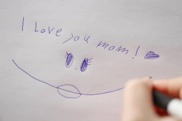 moms day concept. I love you mom inscription on a white sheet and a childs hand with a pen.Holiday of all mothers