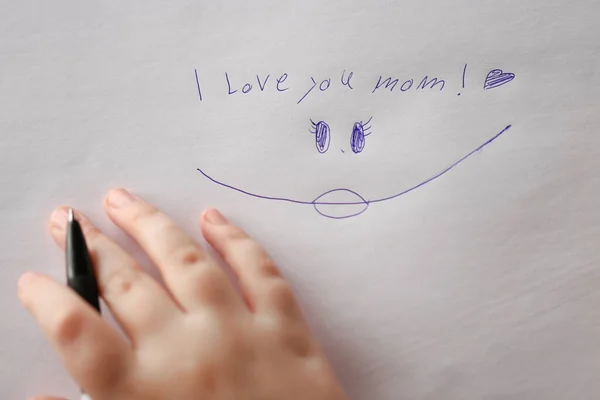 Mothers day holiday. I love you mom inscription on a white sheet and a childs hand with a pen.Holiday of all mothers