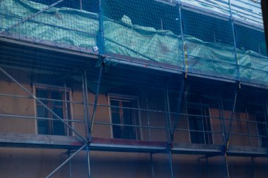 Ev inşaatı. İnşaat ve onarım. Koruyucu mavi bir şebeke içinde yapı iskelesi. Hazırlık binası işi. İnşaat malzemeleri ve bir evin onarımı.. 