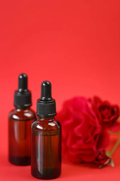 Rose oil. Organic rose oil in brown glass bottles set and red rose on red background. Aromatherapy and cosmetics concept.