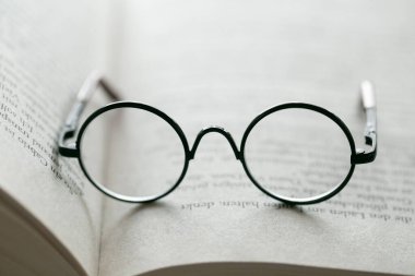 Arka planda bulanık bir ışık üzerine bir kitabın sayfalarında okuma gözlüğü. Eğitim ve okul kavramı.