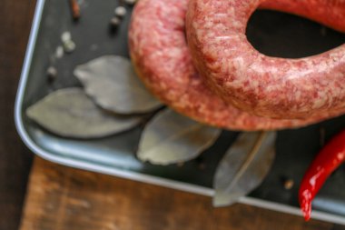  Sosis yakın plan. Çiğ ev yapımı sosis halkaları, koyu ahşap bir masada siyah bir tabakta kırmızı biber. Bitkiler ve sebzelerle lezzetli meze ürünleri.