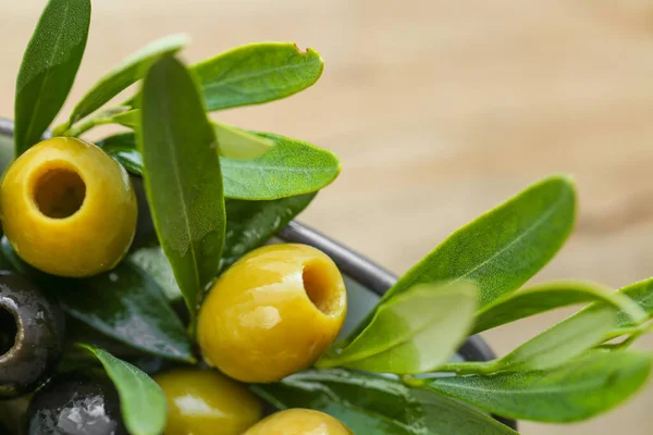 mediterranean cuisine ingredient. Black and green olives and a green olive branch close-up in olive oil on a wooden table. Fresh bio organic olives and black olives.