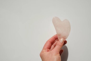 Gua sha facial massage device. gua sha scraper in the shape of a heart made of rose quartz in a female hand on a light background.beauty devices. massager made of pink natural stone
