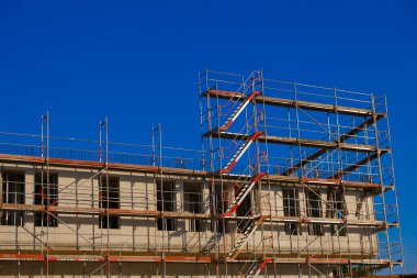 Construction of real estate and industrial premises concept.New house in scaffolding on blue sky background.Building materials and the process of building a new house.Home construction.
