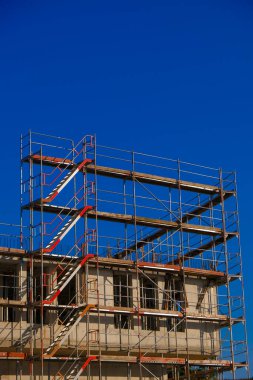 Construction of real estate and industrial premises concept.New house in scaffolding on blue sky background.Foundation and walls of the house in scaffolding.