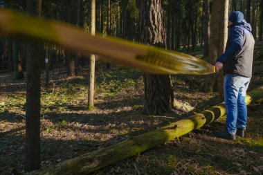Entry ban. Crime scene. No entry. stop motion tape. Man pulling yellow barrier tape in pine dark forest. Murder and crime concept.