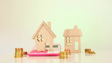 Real estate price.Houses and apartments cost.Mini houses,calculator and coins on a pink light background