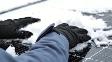 Kışın güneş enerjisi. Kardan güneş panellerini temizliyorum. Ellerinde siyah eldivenler var. Kışın güneş panelleriyle elektrik alıyoruz. 4k görüntü