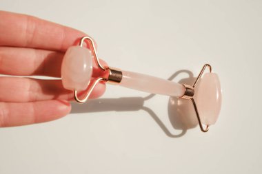 gua sha roller made of quartz in a female hand on a light background.beauty devices.Gua sha facial massage device.Roller massager made of pink natural stone