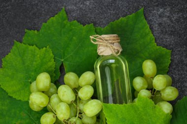 Grape seed oil.grape vinegar. Oil in a transparent bottle and green grapes with leaves on a gray slate background.organic oils.Base cosmetic oil for massage and care for face and body.