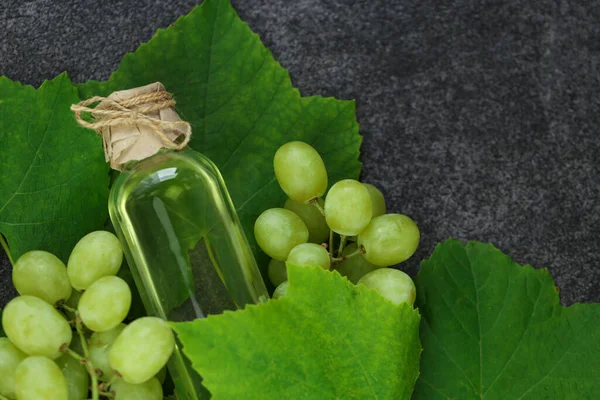 Grape oil.grape vinegar.Oil in a bottle and grapes with leaves on a gray slate background.organic oils.Base cosmetic oil for massage and care for face and body.