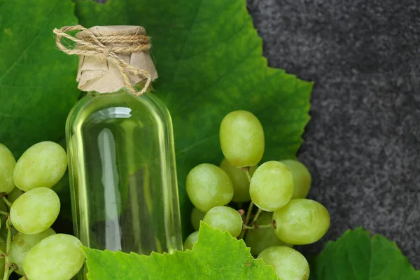 Grape oil.grape vinegar.Oil in a transparent bottle and grapes with leaves on a gray slate background.organic oils.Base cosmetic oil for massage and care for face and body.