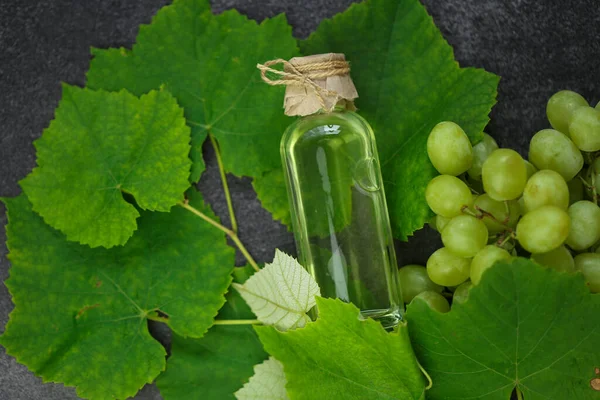 Grape oil.grape vinegar. Oil in a transparent bottle and green grapes with leaves on a gray slate background.organic oils.Base cosmetic oil for massage and care for face and body.