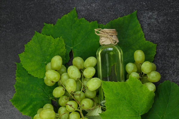 Grape oil.grape vinegar.Oil in a transparent bottle and grapes with leaves on a gray slate background.organic oils.Base cosmetic oil