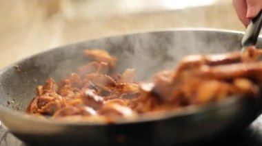 Köri soslu tavuk, dumanlı. Yavaş çekim. Spatula sostaki et parçalarını birbirine yaklaştırıyor. Soslu tavuk eti kızartma tavasında kızarır..