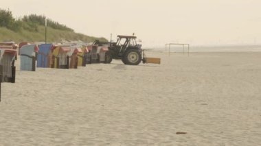 Sahil temizliği. Traktör kumsaldaki kumu eliyor. Sahil temizliği. Deniz sahilindeki kumların saflığı. Almanya. Frisian Adaları. Fer Adası. 4k görüntü