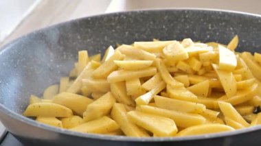 Kızarmış patatesler. Siyah spatula patatesleri külotun içinde çevirir. Güneş ışınlarında patatesin yağı ve buharı. Lezzetli karbonhidrat. 4k görüntü