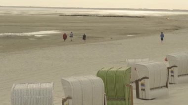 Wadden Denizi. Watt kumulları. Kumlu deniz sahilinde yürüyen insanlar. Deniz eğlencesi ve tatil. Gıdıklanmış Kuzey Alman Denizi 'nin kumlu tabanı boyunca yürüyor. Fer Adası. Almanya 'nın Frizya Adaları