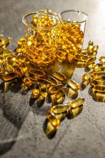 stock image Fish oil capsules in transparent laboratory flasks on a black slate background in bright hard light 