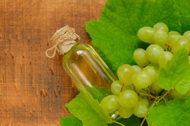 Tahta zeminde üzüm tohumu yağı şişesi ve yeşil üzüm. Masaj ve yüz ve vücut bakımı için temel kozmetik yağı. Organik Doğal Biyolojik Üzüm Tohumu Yağı