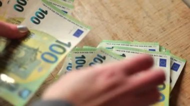 Tahta bir masa üzerinde 100 euro banknotlar. Avro banknotları sayılıyor. Eller banknotları yeniden hesaplıyor. Avrupa ülkelerindeki giderler ve gelirler..