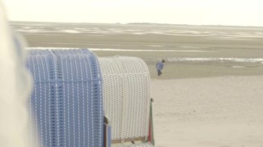 Wadden Deniz Kıyısı. Çocuk bulutlu havada sahilde uçurtma uçuruyor. Plaj aktiviteleri ve eğlence. Kuzey Denizi 'nin sarkık sahillerinde uçurtmalar. Almanya. 4k görüntü