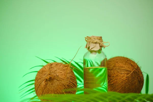 椰子油装在透明的瓶子和椰子里 绿色的棕榈叶在绿色的背景上 蔬菜天然脂肪 — 图库照片