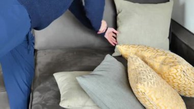 Sofa için yastıklar. Kadın yastıkları yere seriyor. Dur. Eller gri süet kanepeye bir sürü renkli yastık atar. Temizlik ve iç tasarım. 4k görüntü