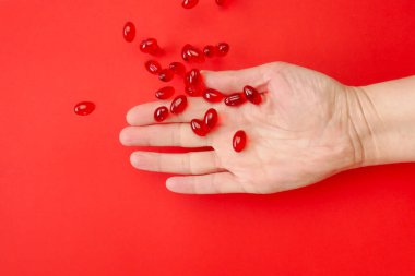 Bir kadının elindeki kril yağı kapsülleri kırmızı zemin üzerinde. Omega yağ asitleri. Uçan jelatin kırmızı kril yağ kapsülleri. Doğal takviyeler ve vitamin. 