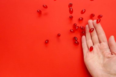 Krill yağ kapsülleri. Omega yağ asitleri. Kırmızı arka planda bir kadının elinde uçan kırmızı kril yağ kapsülleri. Doğal takviyeler 