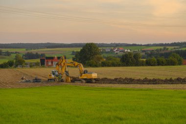 Boru döşeme. Köyün arka planında kazıcılar var. İnşaat makineleri ve inşaat alanında çalışıyor. İletişim yürütülüyor.