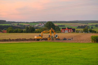 Boru döşeme. Köyün arka planında kazıcılar var. İnşaat makineleri ve inşaat alanında çalışıyor. Özel sektörde haberleşme yürütülüyor.. 