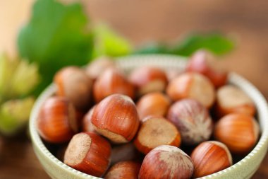 Yuvarlak yeşil bir kasede fındıklar ve ahşap bir masanın üzerinde yeşil yapraklar. Olgun fındık çiftliği. Fındık bolluğu. Organik biyolojik fındık. Yeşil yapraklı fındık. 